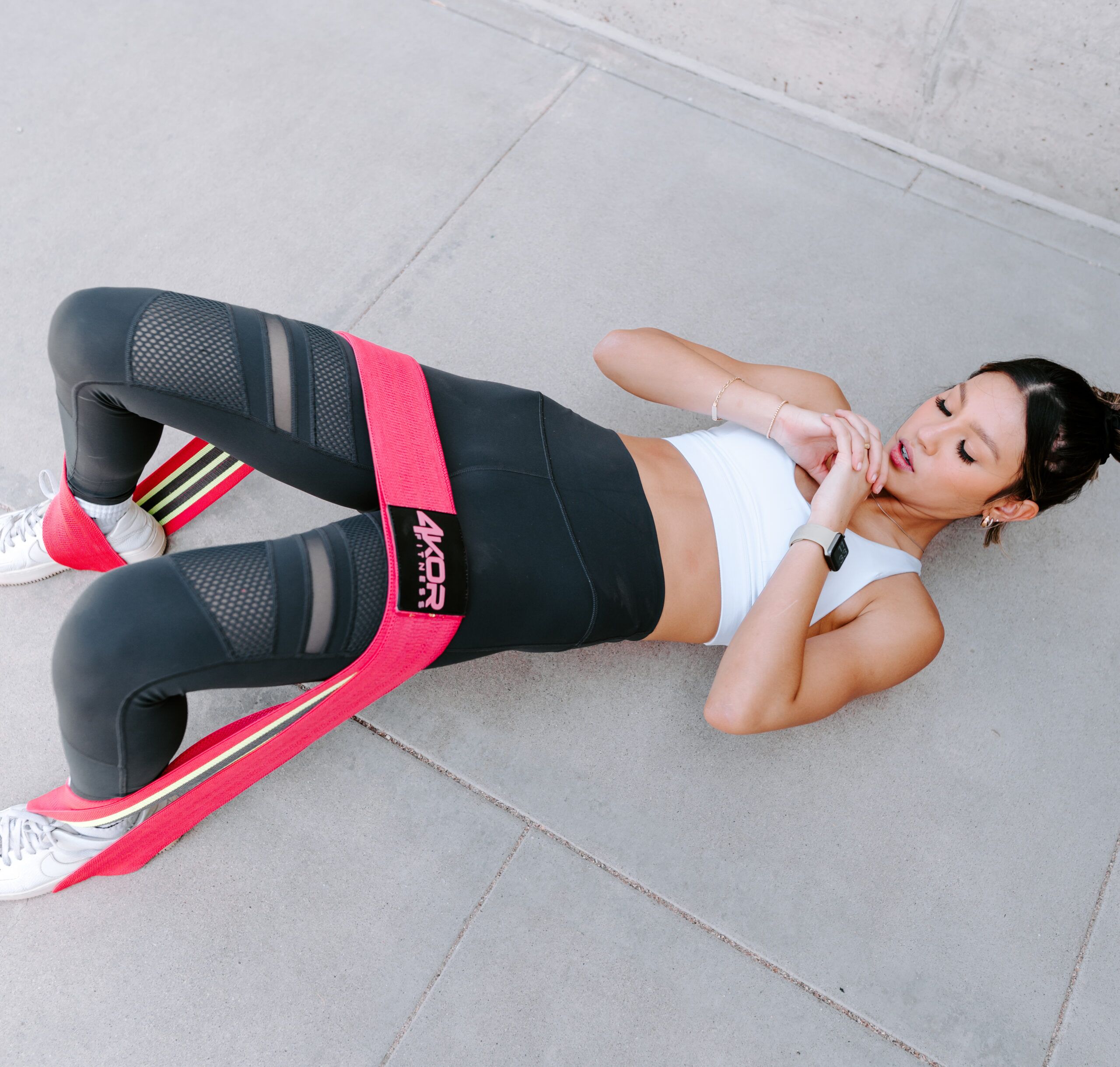 Female athlete in 4KOR Fitness leggings performing a glute bridge with pink long resistance band around thighs, overhead angle