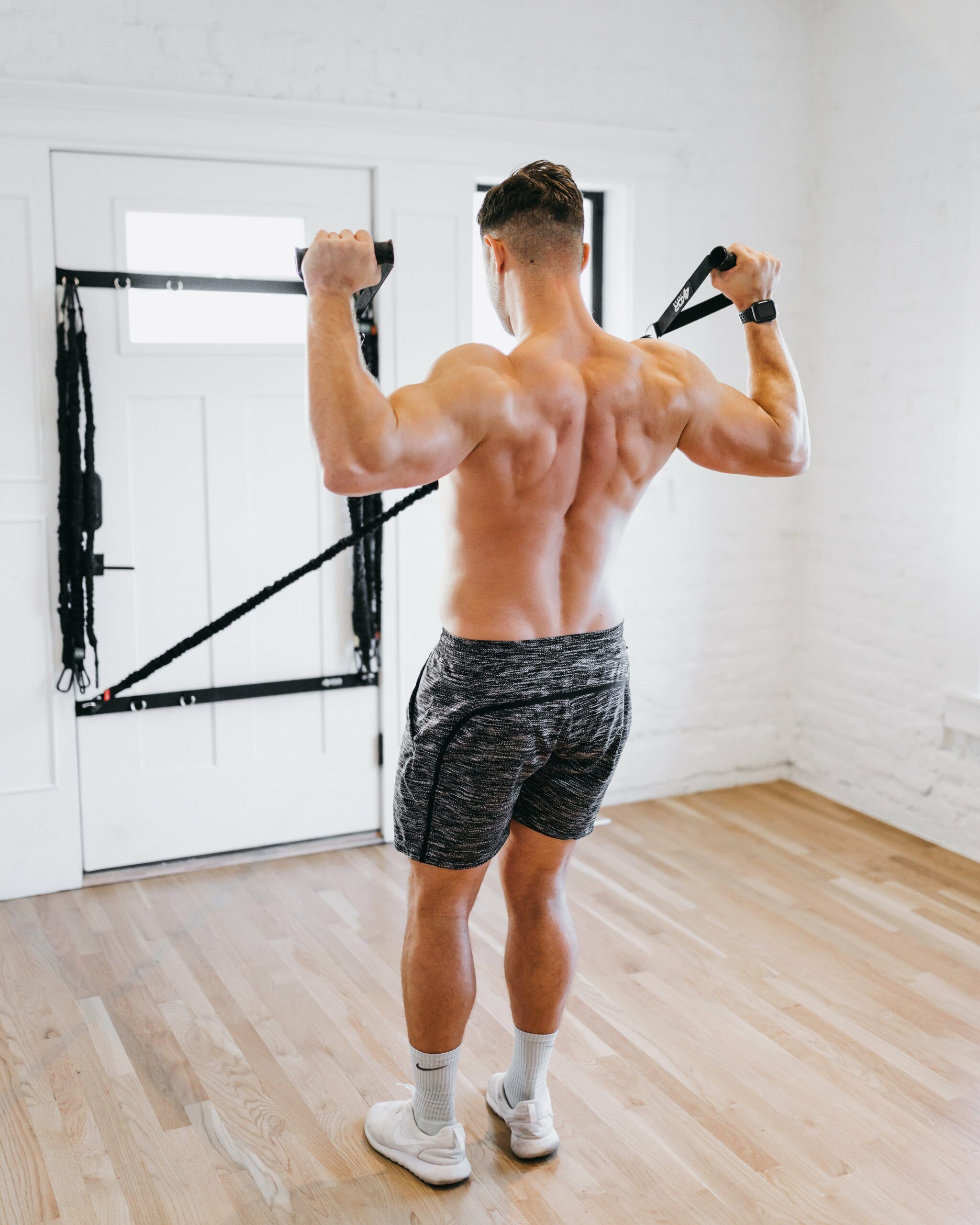 Male athlete performing overhead row with 4KOR Fitness resistance cords anchored to door frame in home studio for back and shoulder training
