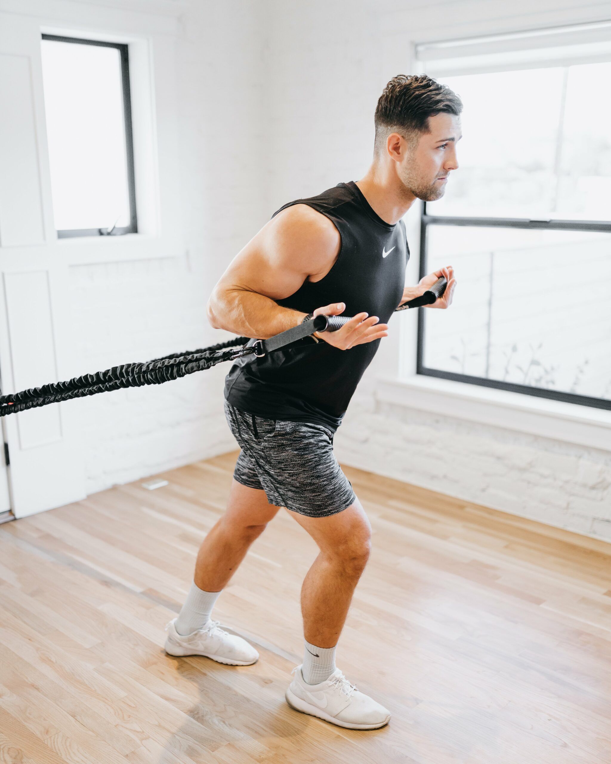 Male athlete performing resistance cord row with 4KOR Fitness exercise handles in bright home studio for back and shoulder training