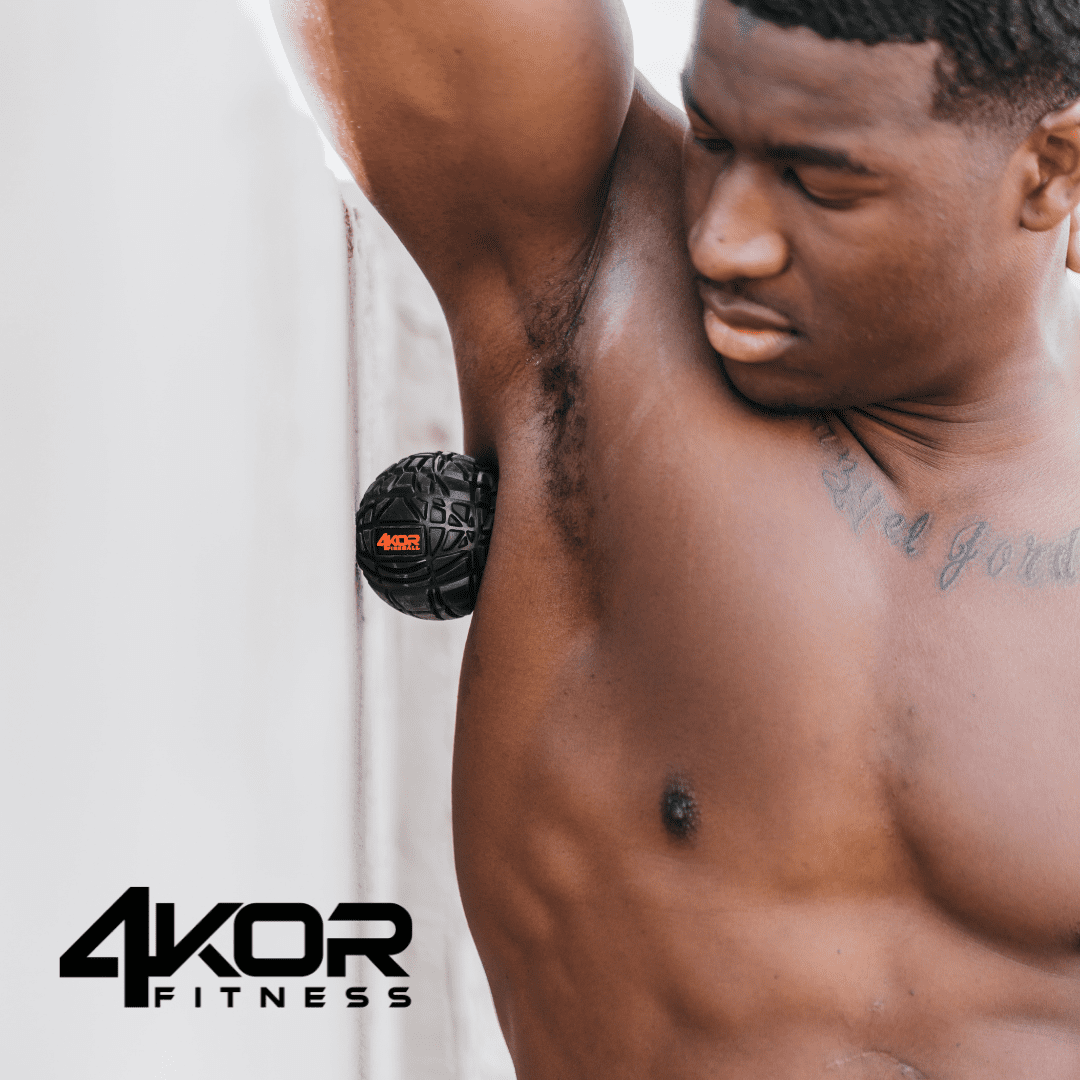 Shirtless male athlete pressing black 4KOR Fitness Fireball massage ball against armpit and lat against wall for targeted myofascial release