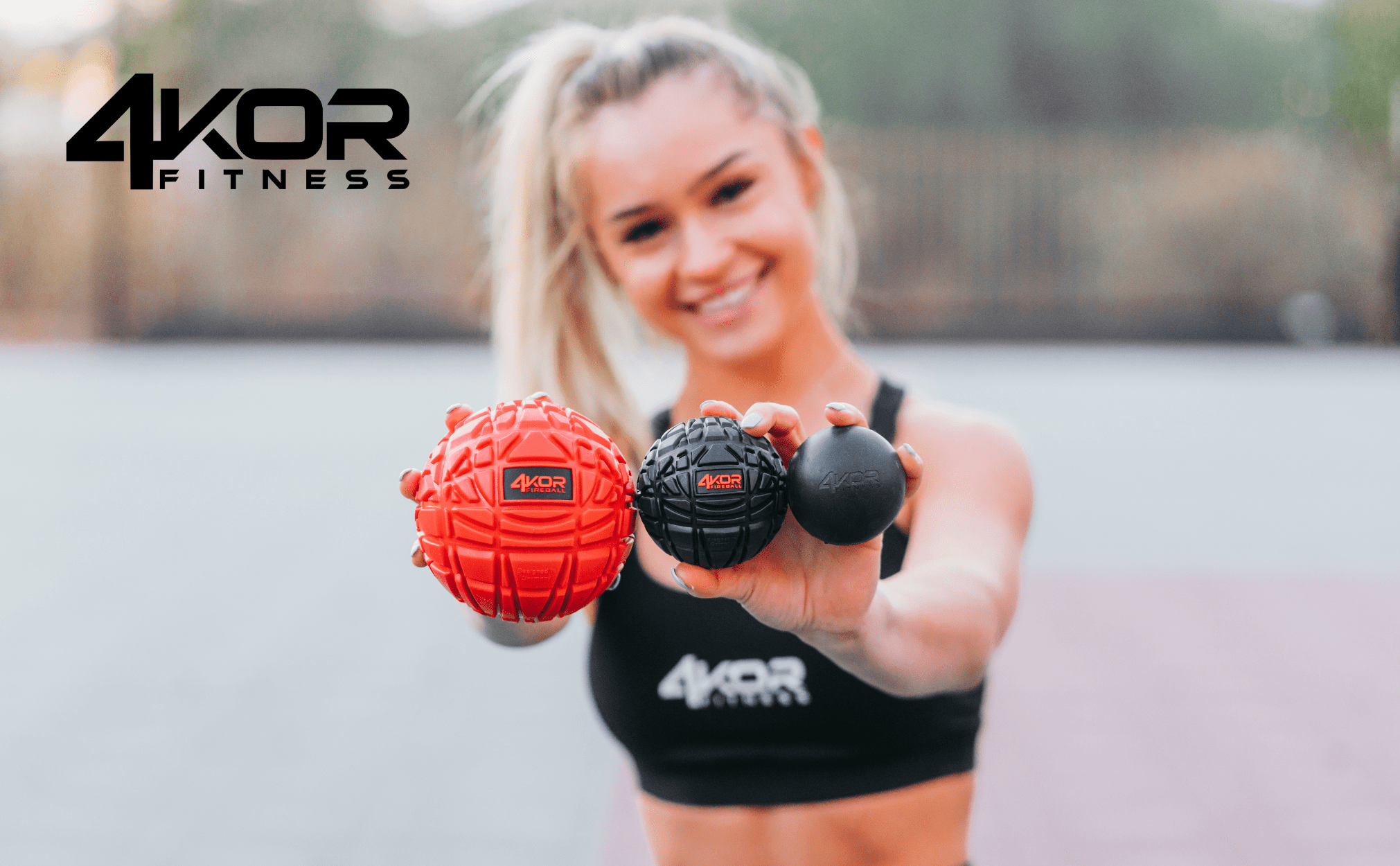 Female athlete in black 4KOR Fitness sports bra holding three Fireball massage balls toward camera, large red, medium black, small black